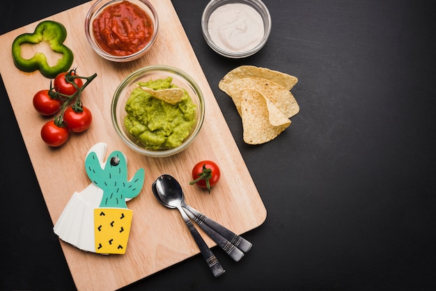 Sauces and vegetables on cutting board near nachos