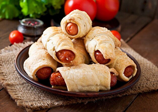 Sausage in the dough sprinkled with sesame seeds on a wooden background in rustic style