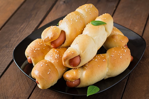 Sausage in the dough sprinkled with sesame seeds on a wooden table in rustic style