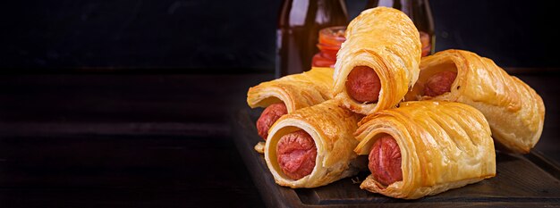 Sausage in the dough on a wooden board with tomato sauce.