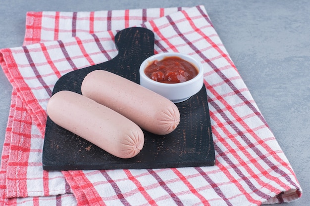 Free photo sausage and ketchup on black cutting board.