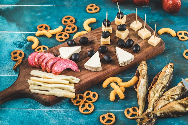 블루 테이블에 마른 생선 나무 보드에 치즈 큐브, 올리브와 크래커와 소시지 조각