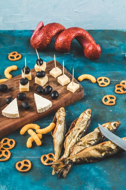 Sausage slices with cheese cubes, olives and crackers on a wooden board with dry fish