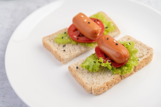 Salsiccia con pomodori, insalata e due set di pane su un piatto bianco.