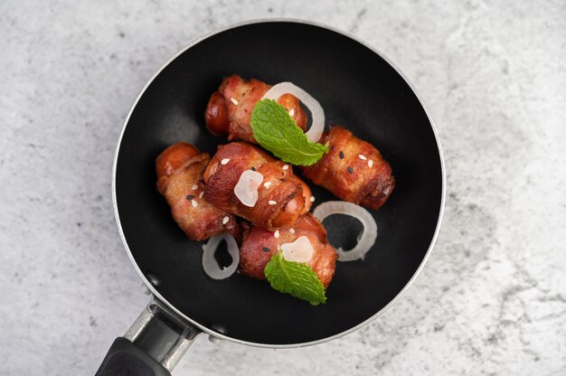 Sausage wrapped in pork belly in a frying pan.