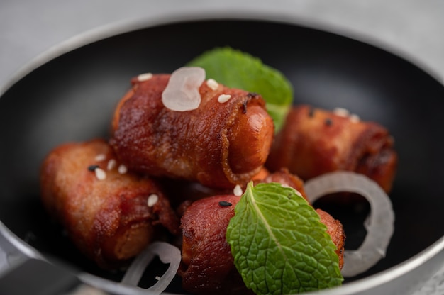 Free photo sausage wrapped in pork belly in a frying pan.