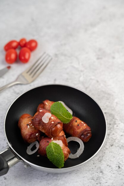 Sausage wrapped in pork belly in a frying pan.