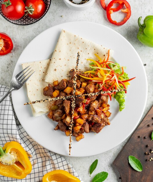 SautÃ©ed meat served with flatbread fresh salad and bread sticks