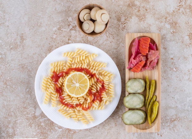 Foto gratuita vassoio di sottaceti salati e ciotola di funghi accompagnati da un piatto di pasta su una superficie di marmo.