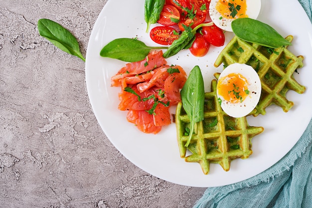 Пикантные вафли со шпинатом и яйцом, помидоры, лосось в белой тарелке. Вкусная еда. Вид сверху. Плоская планировка