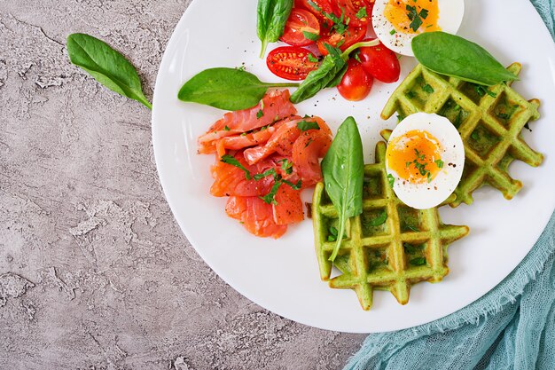 Savory waffles with spinach and egg, tomato, salmon in white plate. Tasty food. Top view. Flat lay