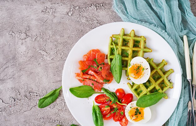 Пикантные вафли со шпинатом и яйцом, помидоры, лосось в белой тарелке. Вкусная еда. Вид сверху. Плоская планировка