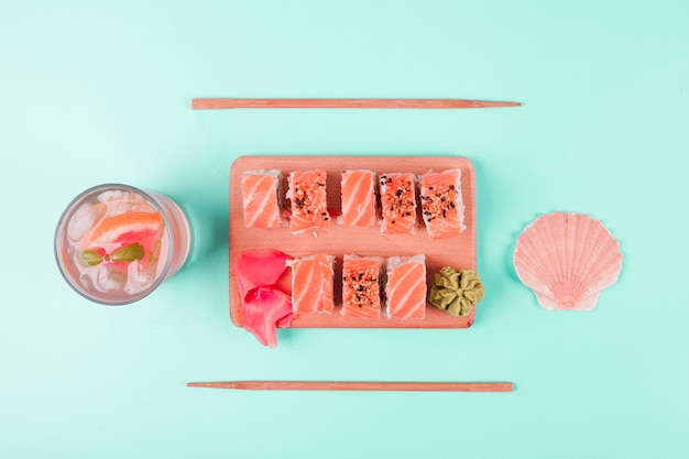 Scallop seashell and grapefruit juice with salmon sushi served with wasabi and pickled ginger on chopping board against mint backdrop