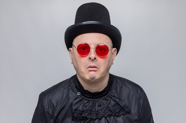 Scared adult slavic man with top hat and with sunglasses in black gothic shirt 