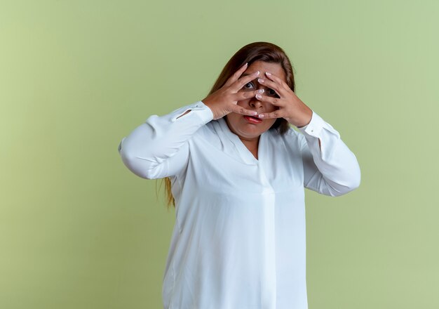 Scared casual caucasian middle-aged woman covered face with hands isolated on olive green wall