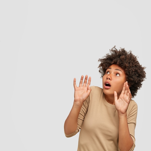 Scared dark skinned young African female keeps hands in protective gesture