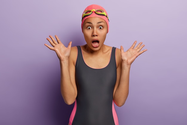 Free photo scared emotional dark skinned woman in swimwear, raises palms, keeps mouth opened from fear