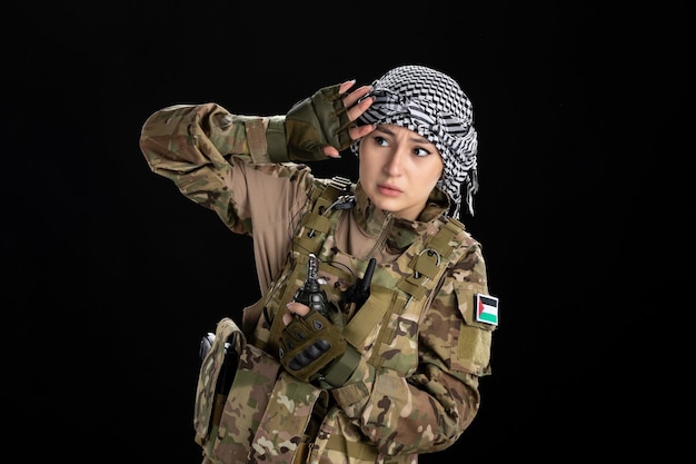 Free photo scared female soldier in military uniform with grenade black wall