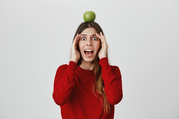 Scared girl scream in panic as seeing flying arrow, holding apple target on head