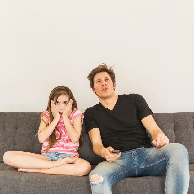 Испуганная девушка сидит возле своего отца на диване