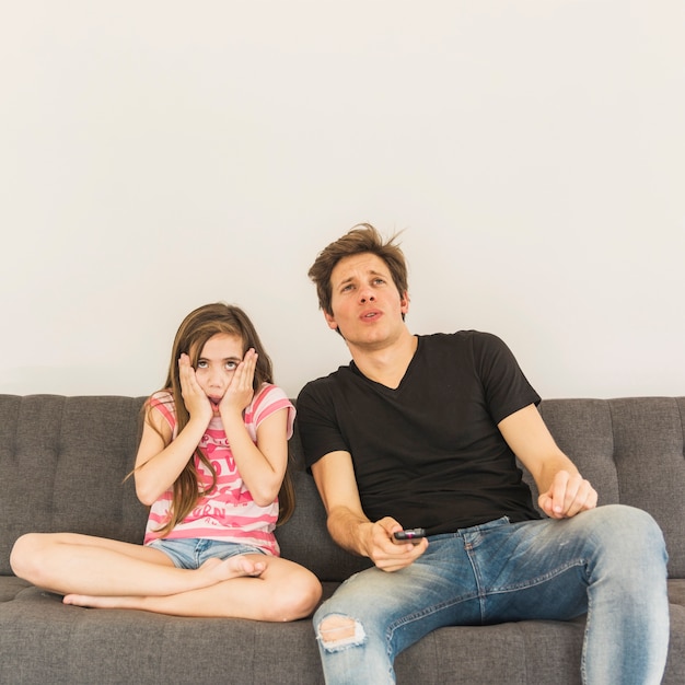 Scared girl sitting near her father on sofa
