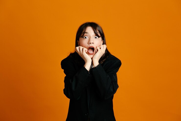 オレンジ色の背景で隔離の黒いジャケットを着て怖いつかんだあご若い美しい女性