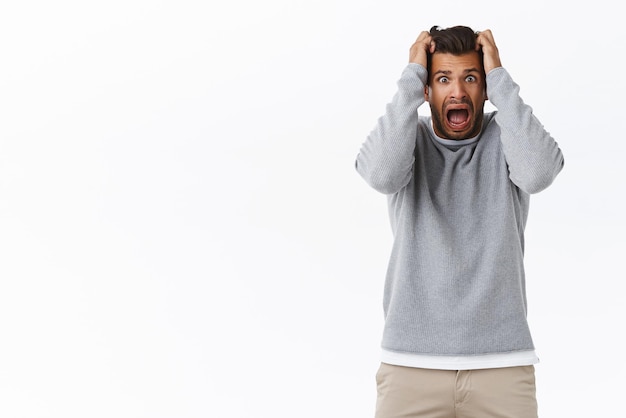 Free photo scared guy in panic grab head and screaming stare camera popped eyes from fright afraid something trembling fear standing stupor shouting terrified standing white background frustrated