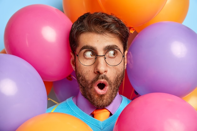 Scared guy surrounded by party balloons posing