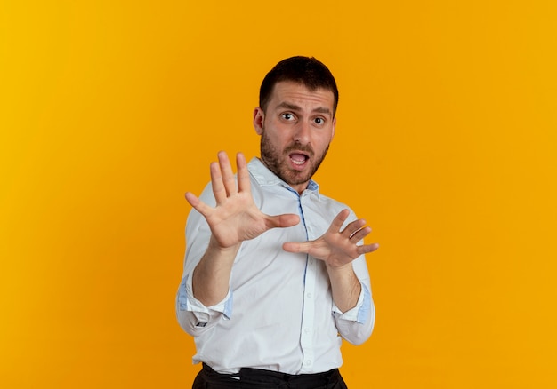 Scared handsome man pretends to defend with hands isolated on orange wall