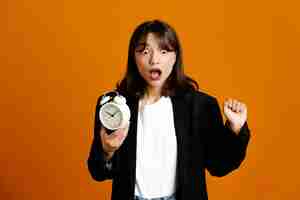 Free photo scared holding alarm clock young beautiful female wearing black jacket isolated on orange background 33