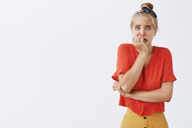 Scared and insecure young blond girl posing against the white wall