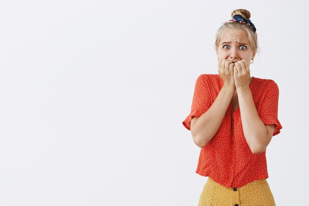 Scared and insecure young blond girl posing against the white wall