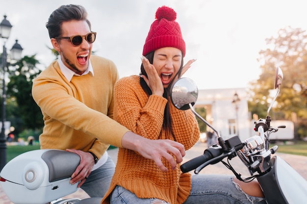 Scared lady in knitted hat sitting on scooter with eyes closed