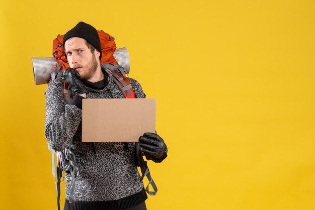 scared male hitchhiker with leather gloves and backpack holding blank cardboard