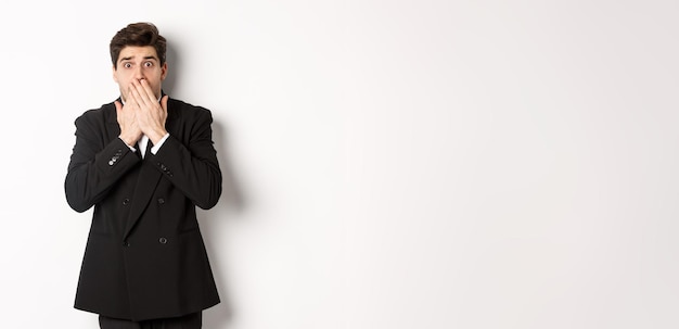 Free photo scared man in formal suit gasping and looking frightened at camera standing against white background