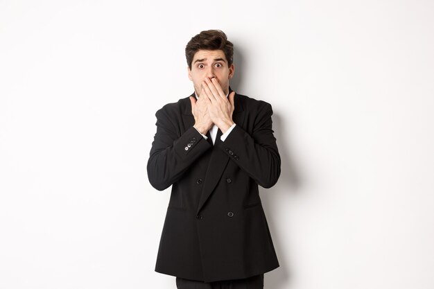 Free photo scared man in formal suit, gasping and looking frightened at camera, standing against white background