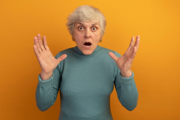 Scared old woman wearing blue turtleneck sweater keeping hands in air