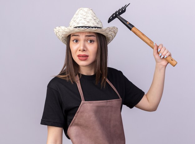 Scared pretty caucasian female gardener wearing gardening hat holding rake