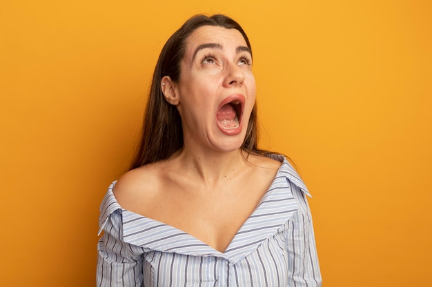 Scared pretty woman looks up isolated on orange wall