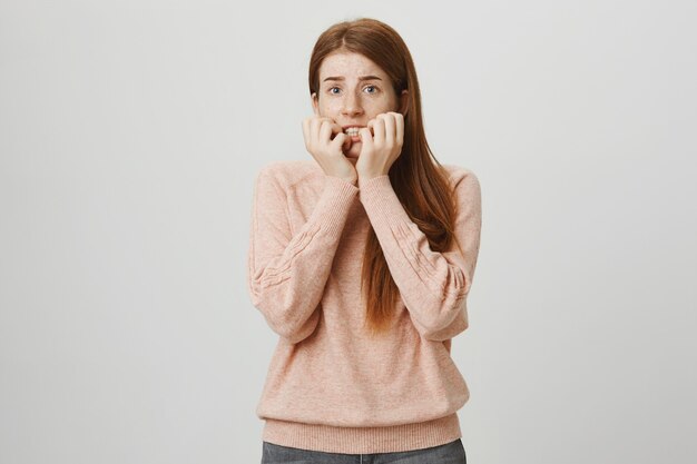 Scared redhead girl biting fingernails, looking frightened