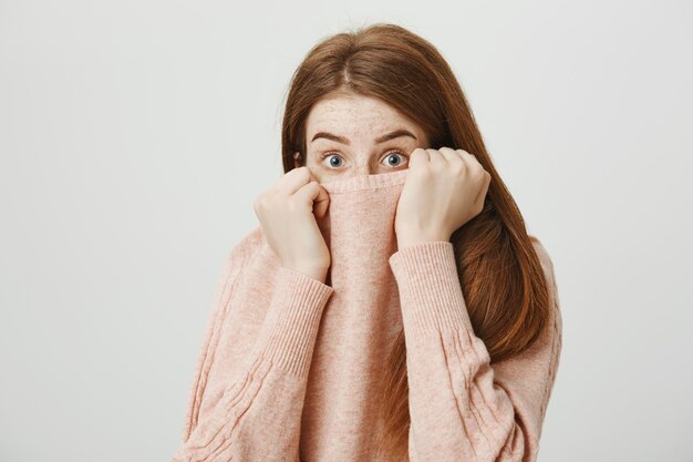 Scared redhead woman hiding face in sweater collar, shivering