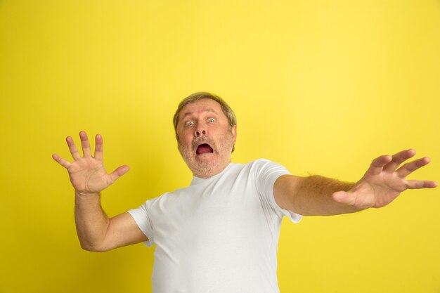 Scared, shocked. Caucasian man portrait isolated on yellow studio background. Beautiful male model in white shirt posing. Concept of human emotions, facial expression, sales, ad. Copyspace.