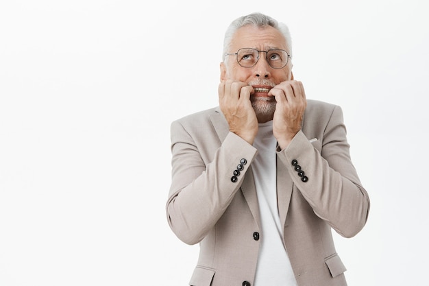 Free photo scared and shocked senior man biting fingernails and looking anxious