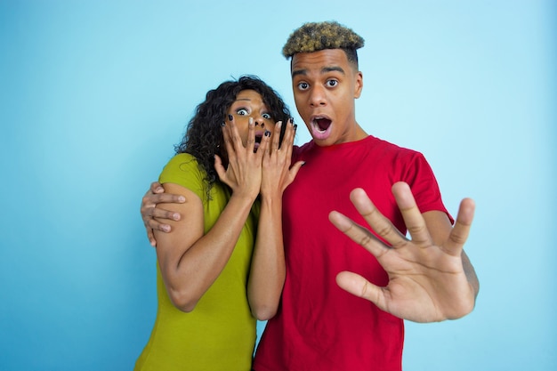 Free photo scared, shocked. young emotional african-american man and woman in colorful clothes on blue wall.