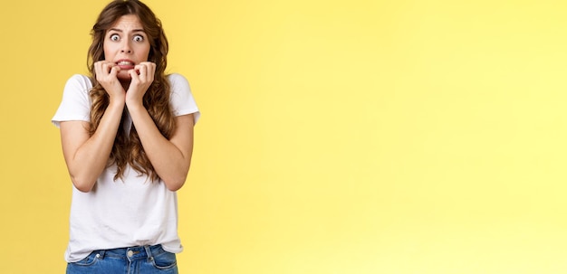 Free photo scared timid insecure unconfident european girl curly haircut hold hands face biting fingers look