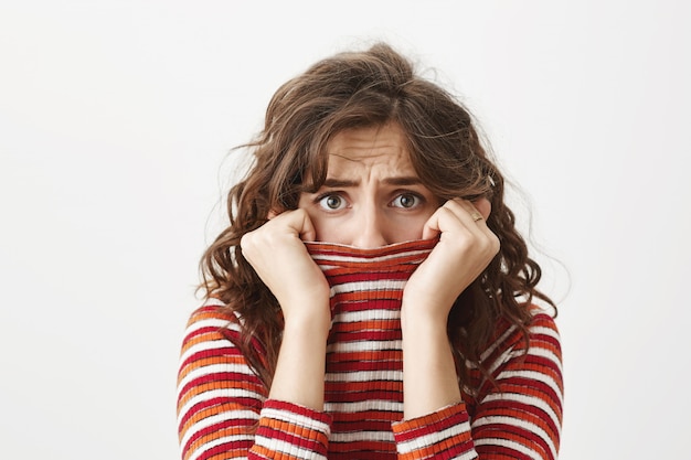 Foto gratuita donna timida spaventata che trema e nasconde il viso all'interno del colletto del maglione