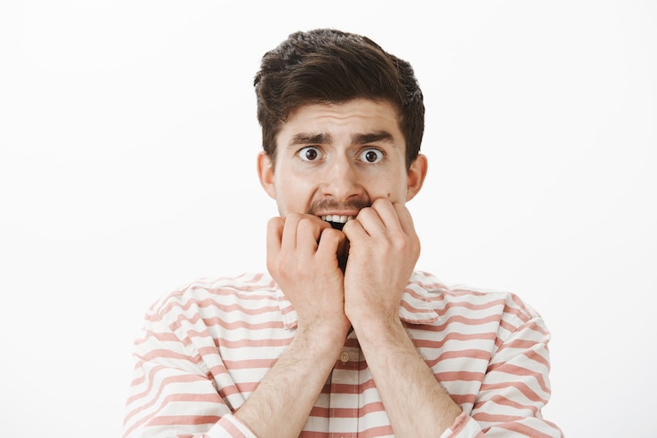 Free Photo scared trembling poor european guy in stripes shirt, biting fingers and staring afraid, being frightened to death, looking scary movie alone in dark, standing over gray wall