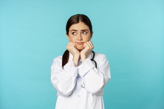 Scared and worried woman doctor in white coat looking anxious and insecure shaking from fear standin...