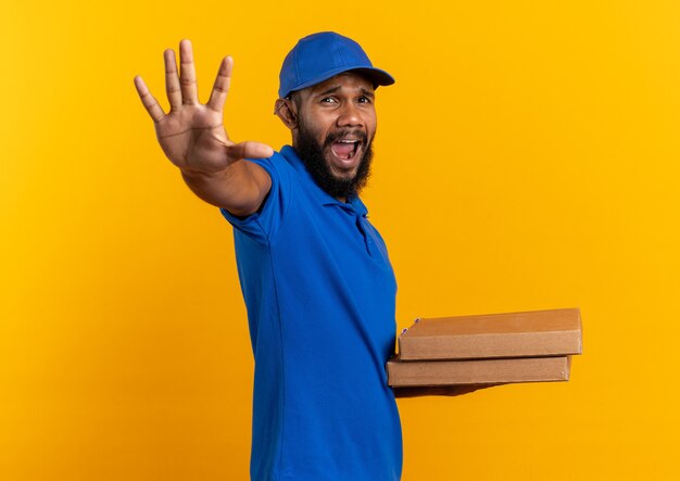 무서워 젊은 아프리카 계 미국인 배달 남자 피자 상자를 들고 복사 공간이 오렌지 벽에 고립 된 손을 뻗어