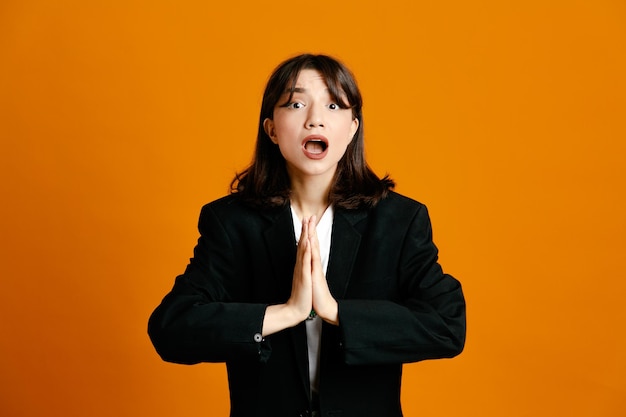 Scared young beautiful female wearing black jacket isolated on orange background